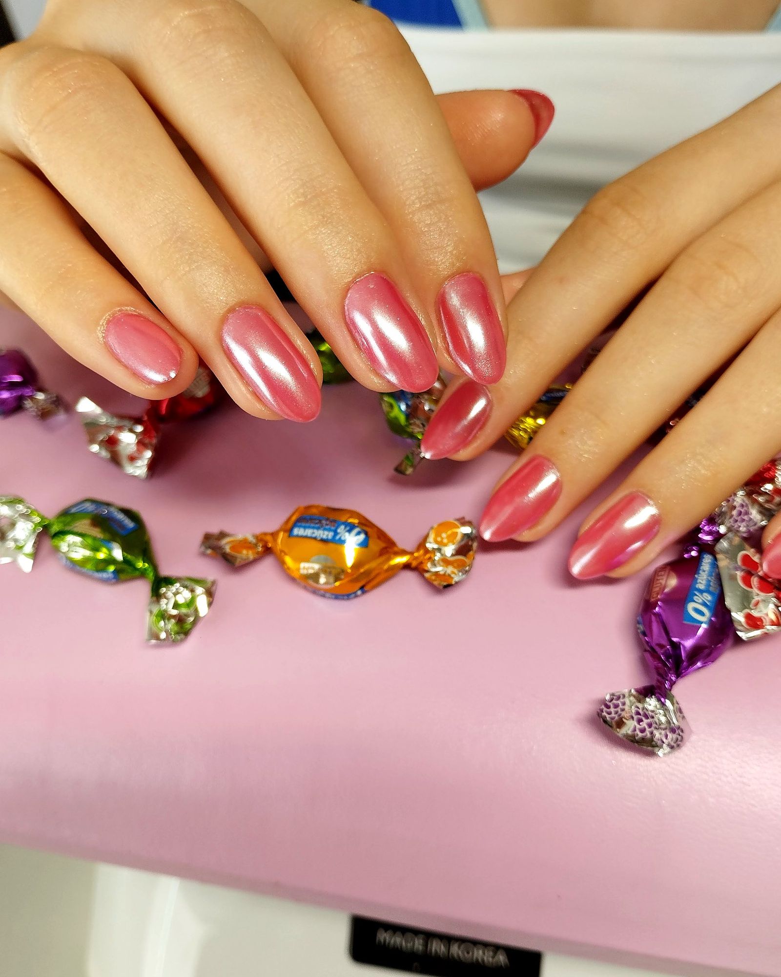 Ungles d'ametla en rosa cromat sobre el coixí de manicura, amb caramels